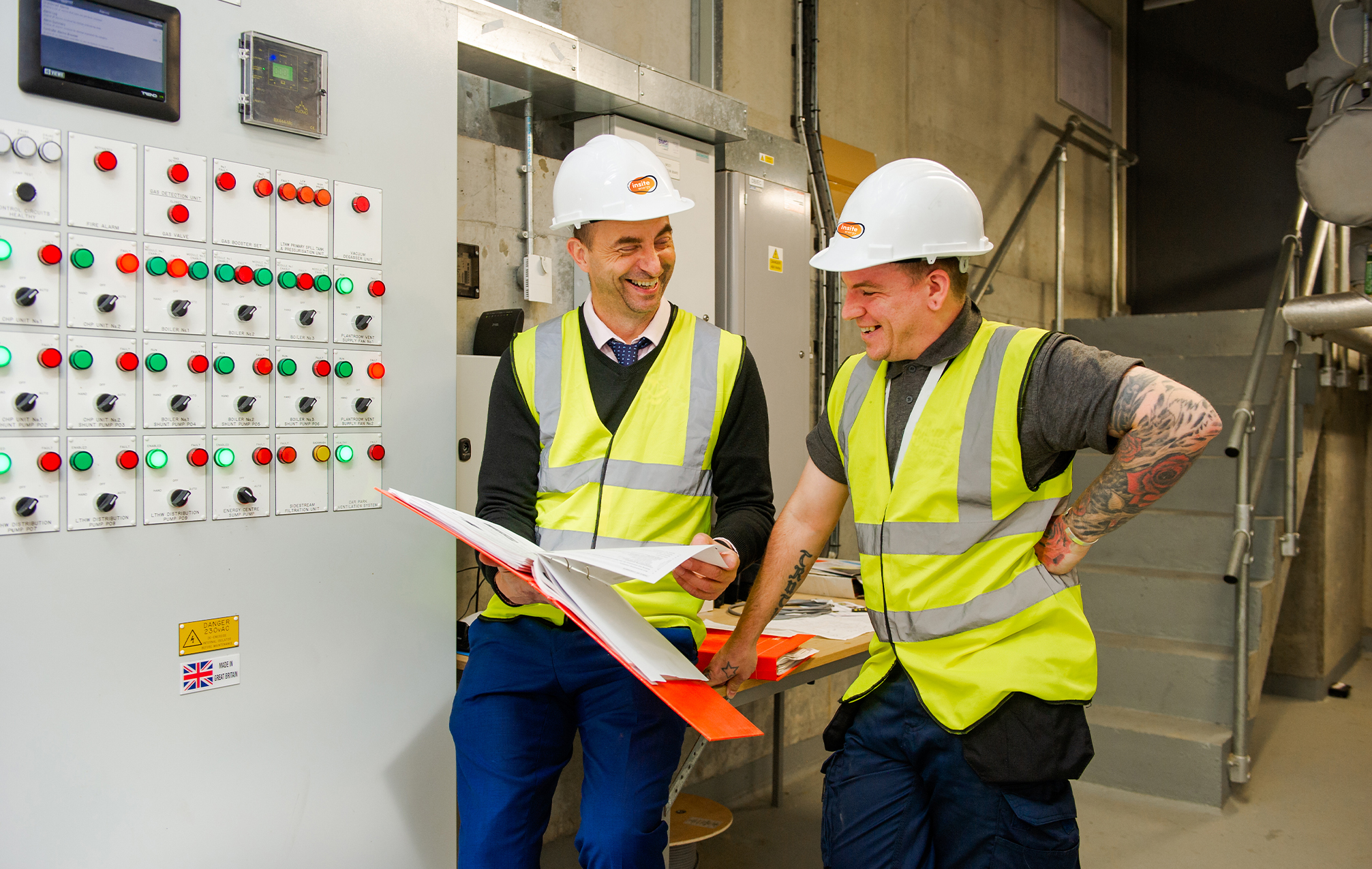 Two engineers reading documents in a folder in a plant room